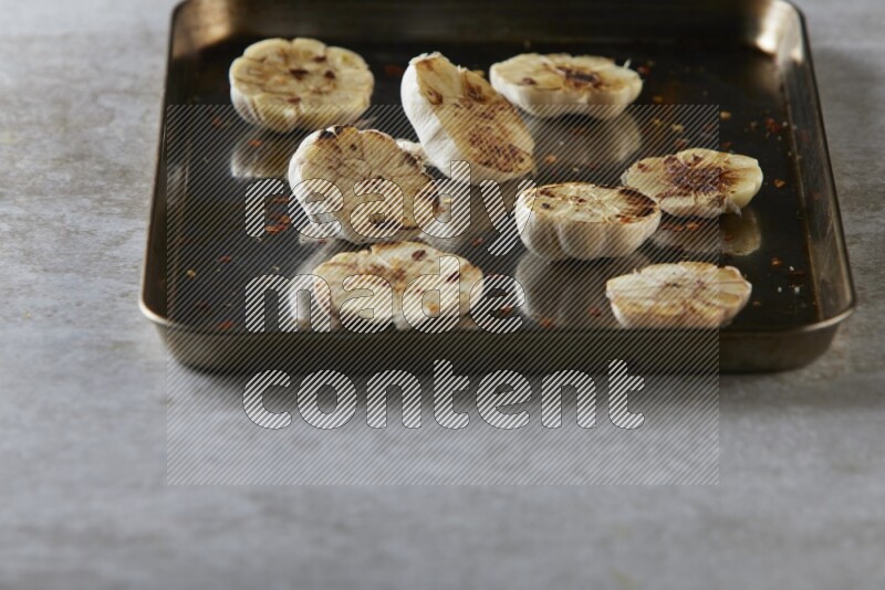 half's roasted garlic in a stainless tray on a grey textured countertop