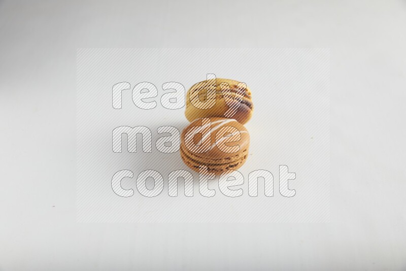 45º Shot of of two assorted Brown Irish Cream, and Yellow Crème Brulée macarons on white background