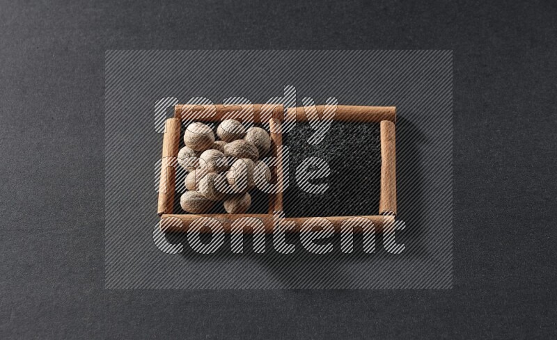 مربعان من أعواد القرفة ممتلئان بحبة البركة السوداء وجوزة الطيب علي خلفية سوداء