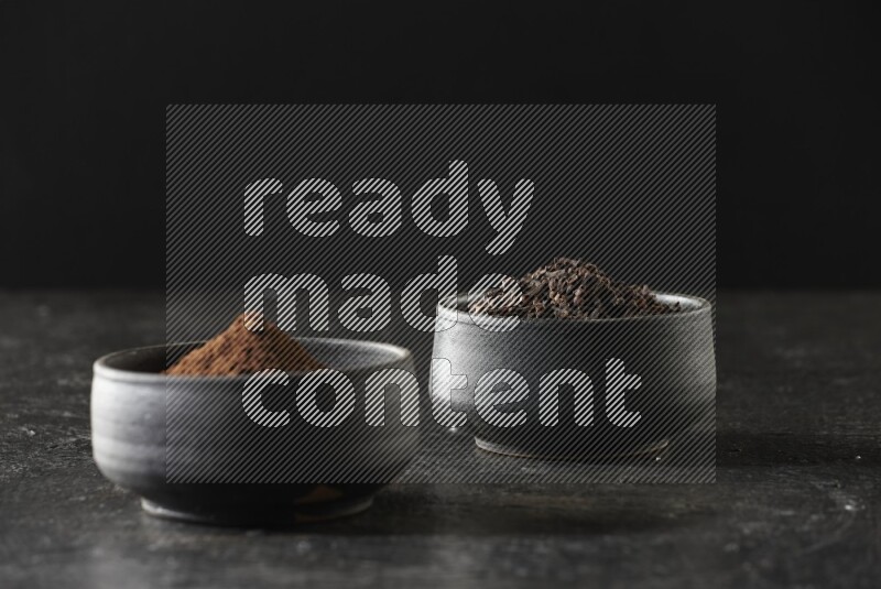 وعاءين من الفخار الأسود أحدهما ممتلئي بحبوب القرنفل والآخر ممتلئ ببودرة القرنفل على خلفية سوداء