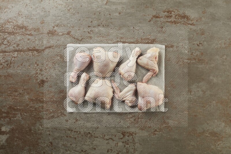 Mixed fresh chicken pieces on a parchment paper direct on a textured rustic background