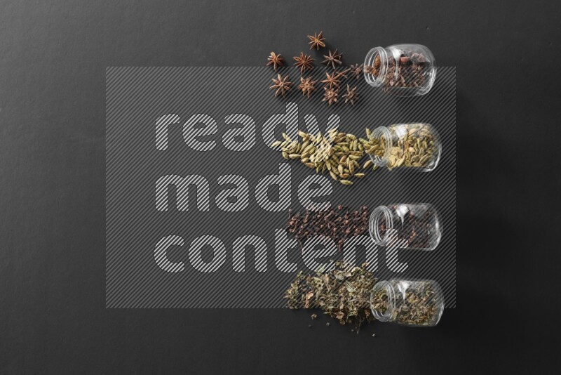 قرنفل وحبوب الهيل وريحان مجفف ويانسون نجمي في أوعية زجاجية علي خلفية سوداء