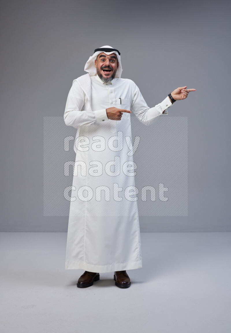 Saudi man Wearing Thob and white Shomag standing interacting with the camera on Gray background