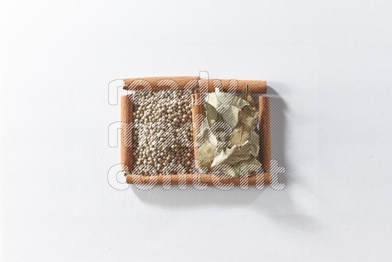 مربعان من أعواد القرفة ممتلئان بحبوب الفلفل الأبيض وأوراق الغار علي خلفية بيضاء