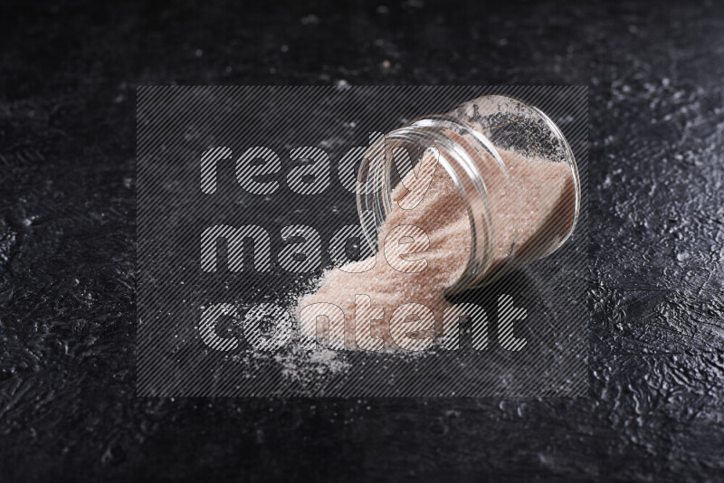 A glass jar full of fine himalayan salt on black background