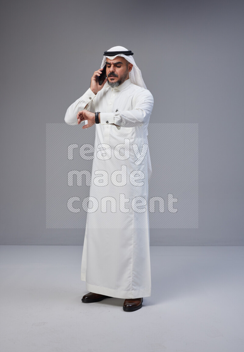 Saudi man Wearing Thob and white Shomag standing talking on phone on Gray background