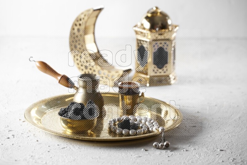 Dried plums in a metal bowl with coffee and prayer beads on a tray beside lanterns in a light setup