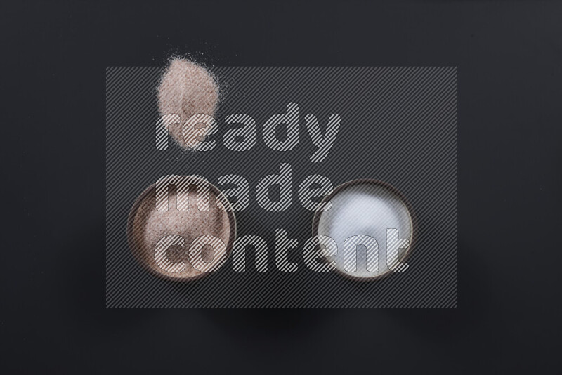 2 وعاء فخاري احدهمها ممتلئ بملح الهيمالايا والأخر بالملح الأبيض على خلفية سوداء