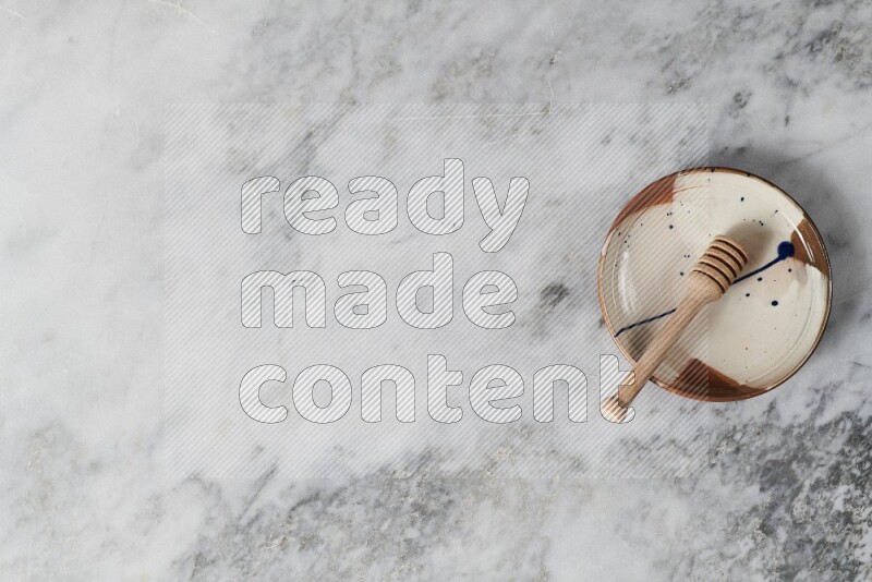 طبق فخاري متعدد الألوان مع ملعقة عسل خشبية بداخله على خلفية من الرخام الرمادي