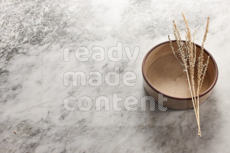 Wheat stalks on beige pottery oven bowl on grey marble background
