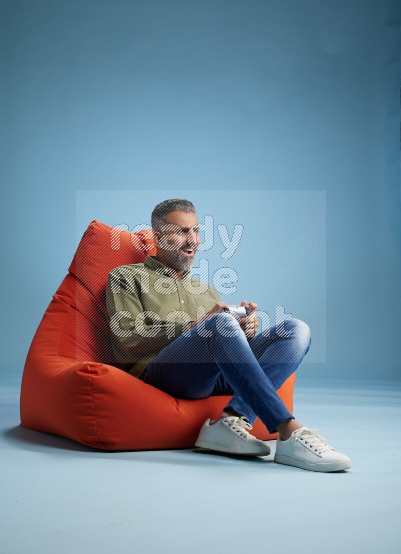 A man sitting on an orange beanbag and gaming with joystick