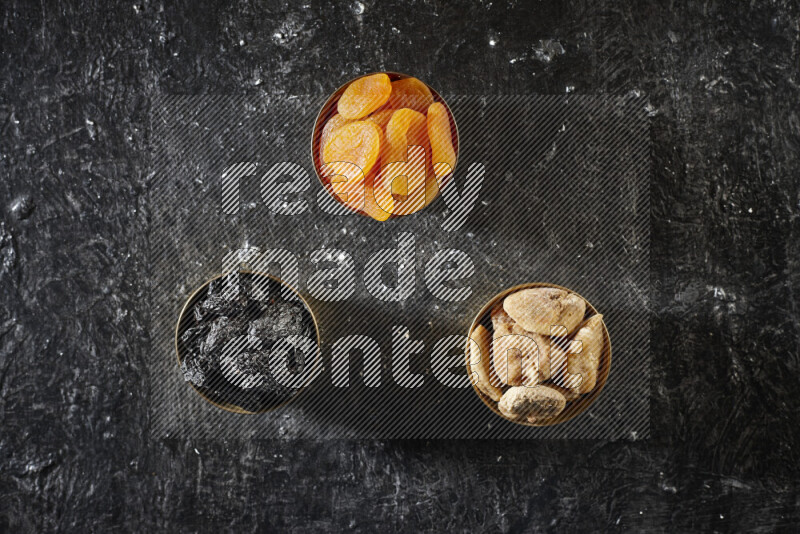 Dried fruits in metal bowls in a dark setup