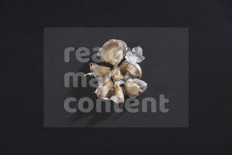 A cracked garlic bulb showing the cloves inside it on a black flooring