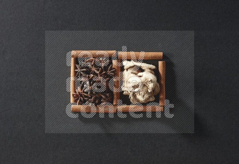 مربعان من أعواد القرفة ممتلئان باليانسون النجمي والزنجبيل المجفف علي خلفية سوداء