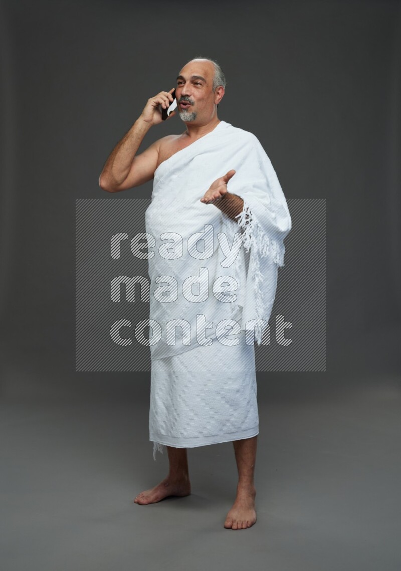 A man wearing Ehram Standing talking on phone on gray background