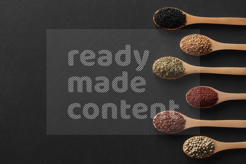 الفلفل الأسود وحبوب الخردل وحبة البركة وحب الرشاد والكمون و حبوب الكتان في معالق خشبية علي خلفية سوداء