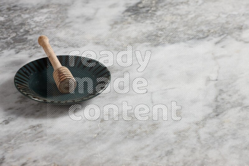 طبق فخاري متعدد الألوان مع ملعقة عسل خشبية بداخله على خلفية من الرخام الرمادي