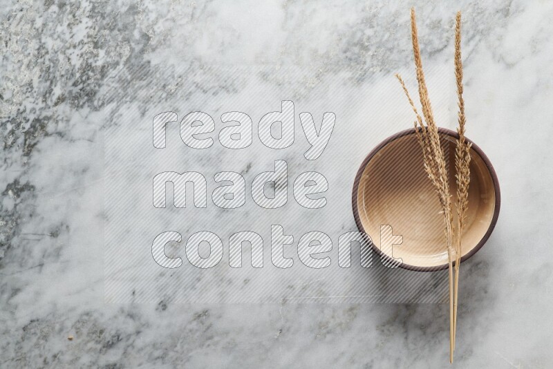 Wheat stalks on beige pottery oven bowl on grey marble background
