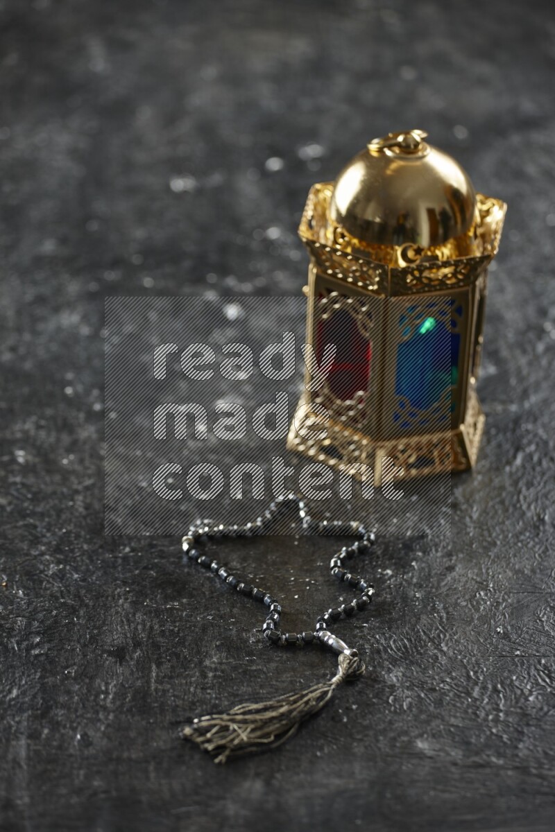 A golden lantern with different drinks, dates, nuts, prayer beads and quran on textured black background