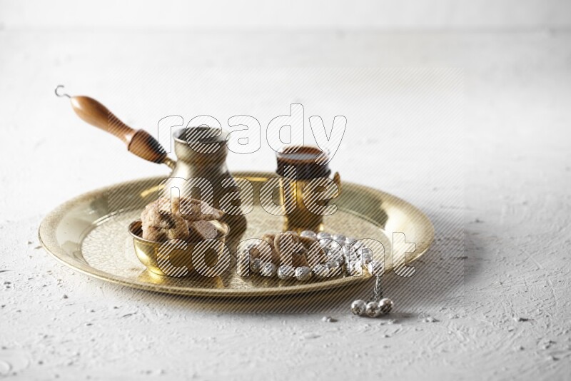Dried figs in a metal bowl with coffee and prayer beads on a tray in a light setup