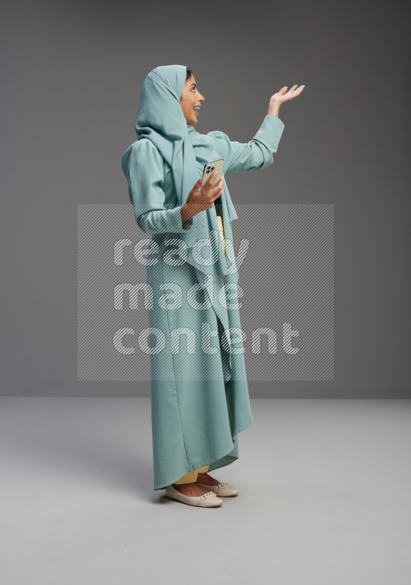Saudi Woman wearing Abaya standing texting on phone on Gray background