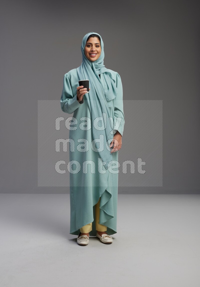 Saudi Woman wearing Abaya standing  holding paper cup on Gray background