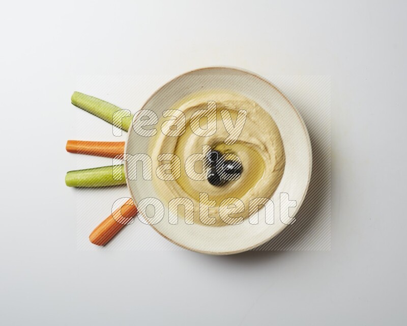 Hummus in a pottry plate garnished with black olives on a white background