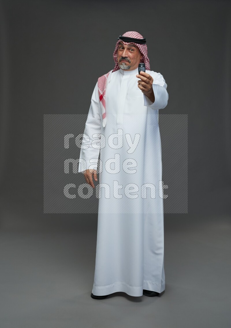 Saudi man with shomag Standing holding car key on gray background