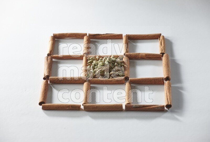 9 squares of cinnamon sticks full of cardamom in the middle surrounded by nutmeg, cinnamon, bay laurel leaves, cloves, cumin, dried ginger, dried basil and star anise on white flooring