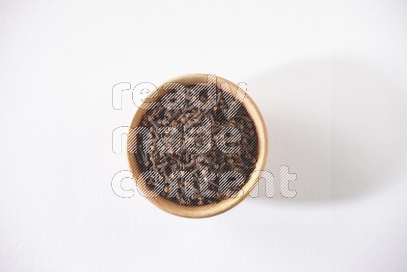 A wooden bowl full of cloves on a white flooring