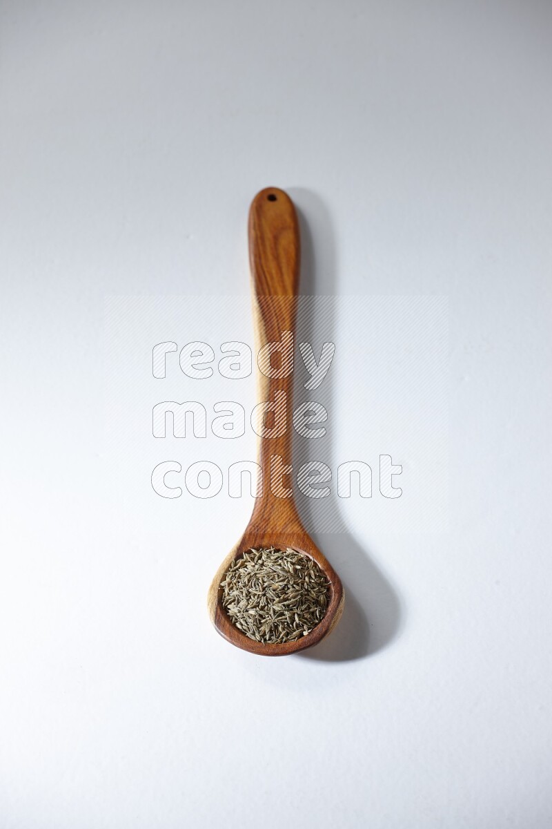 A wooden ladle full of cumin seeds on a white flooring