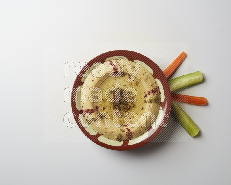 Hummus in a traditional plate garnished with zaatar & sumak on a white background
