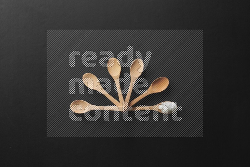 wooden spoons filled with white peppers, cloves, cardamom, salt, black peppers and basil on black flooring