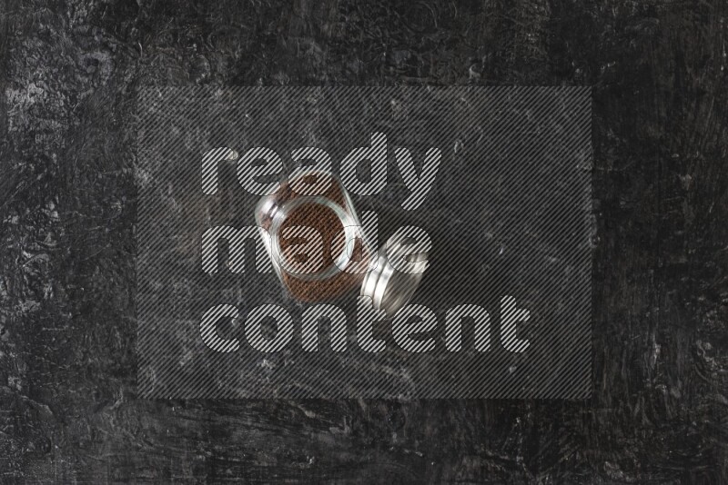 A glass spice jar full of cloves powder on textured black flooring