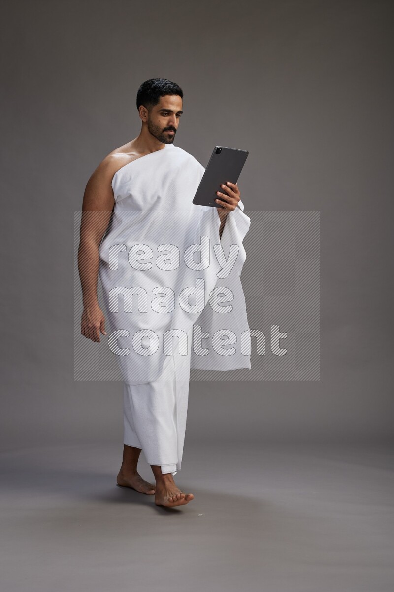 A man wearing Ehram and holding a tablet on gray background
