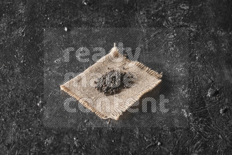 Black pepper on burlap fabric on a textured black flooring