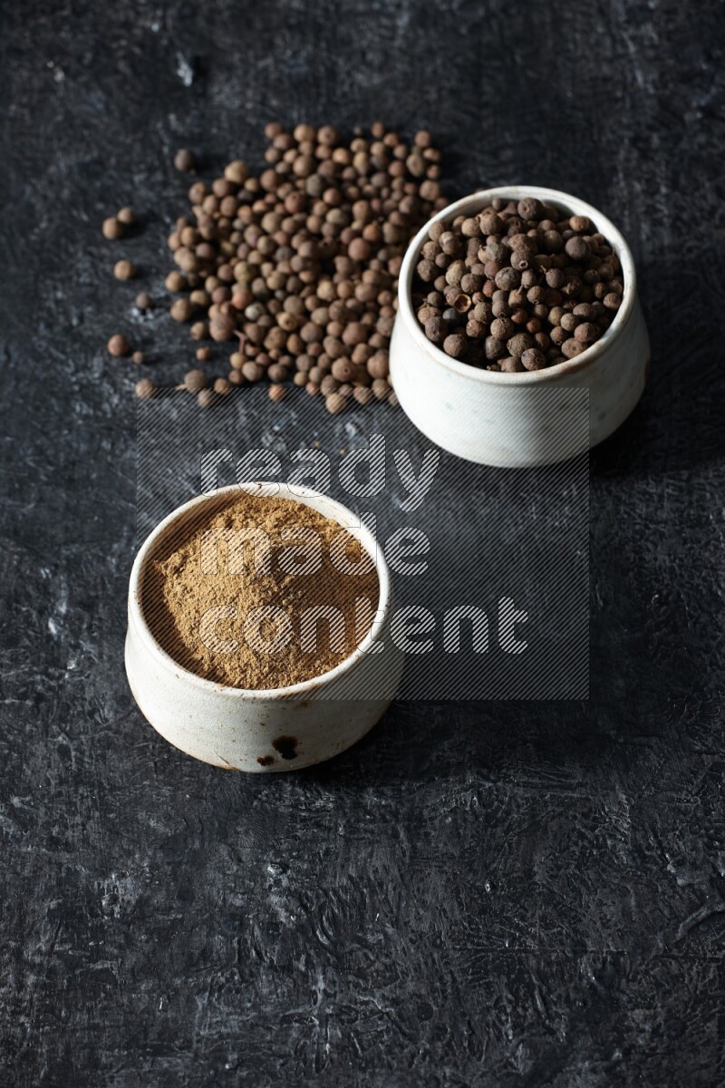 وعاءان بيج، أحدهما ممتلئ ببودرة بهار الفلفل الحلو والآخر بالحبوب وكلاهما متناثران على خلفية سوداء