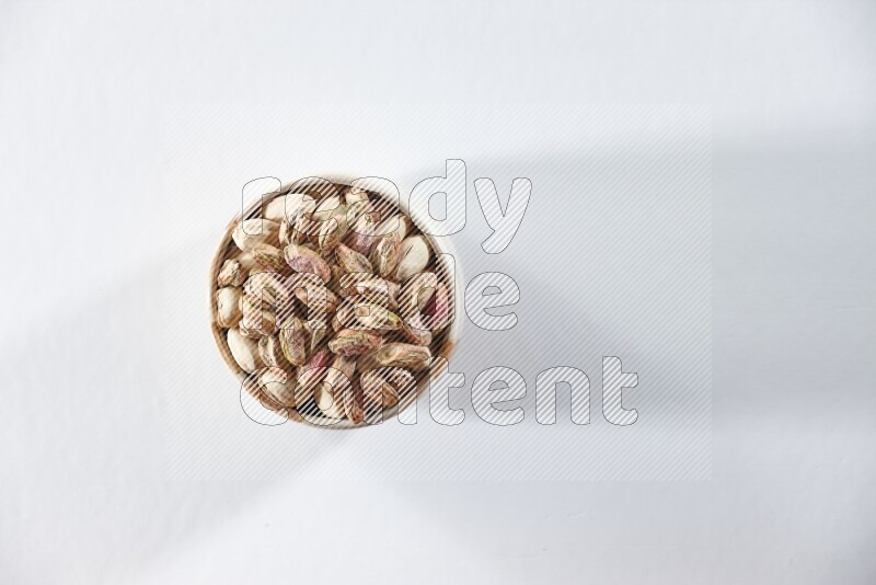 A beige ceramic bowl full of peeled pistachios on a white background in different angles