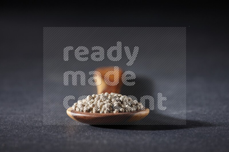 A wooden ladle full of white pepper beads on black flooring