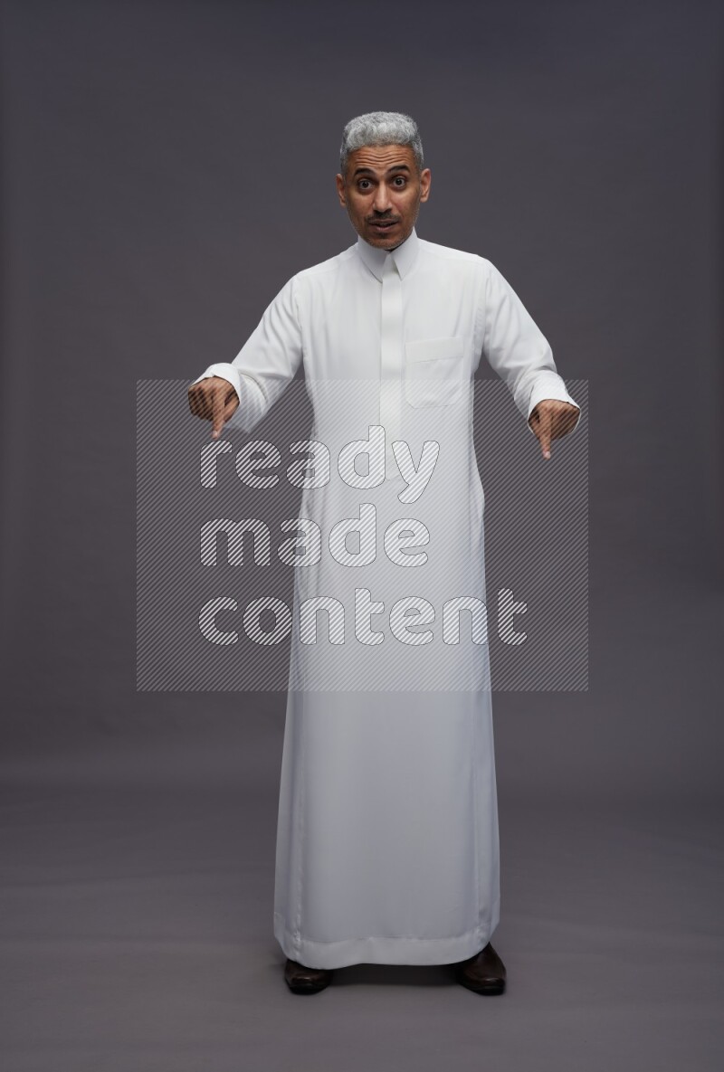 Saudi man wearing thob standing interacting with the camera on gray background