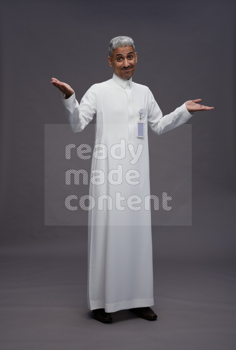 Saudi man wearing thob with pocket employee badge standing interacting with the camera on gray background