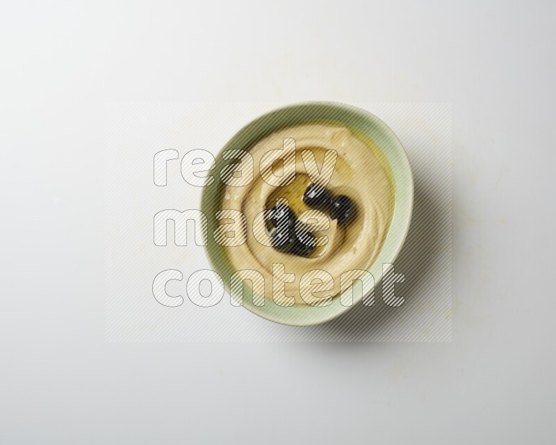Hummus in a green plate garnished with black olives on a white background
