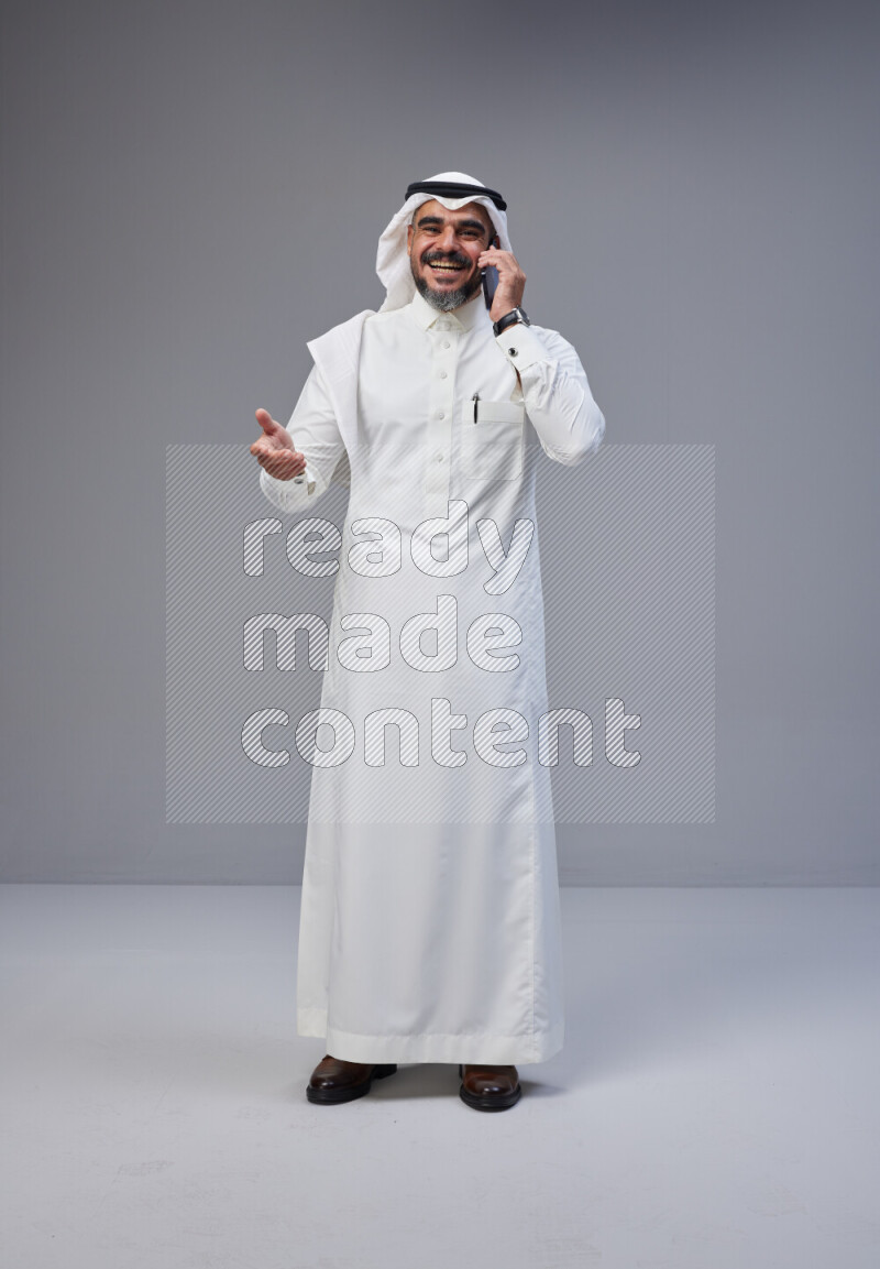Saudi man Wearing Thob and white Shomag standing talking on phone on Gray background