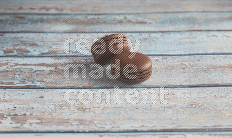 45º Shot of two Brown Dark Chocolate macarons on light blue wooden background