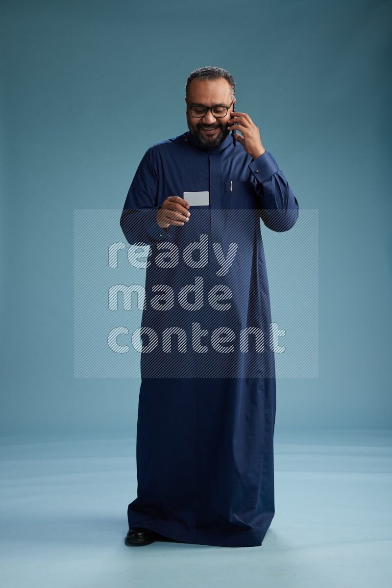 Saudi Man without shimag Standing holding ATM while talking on phone on blue background
