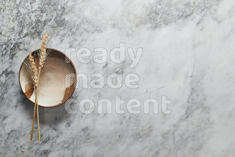 Wheat stalks on multicolored pottery plate on grey marble background