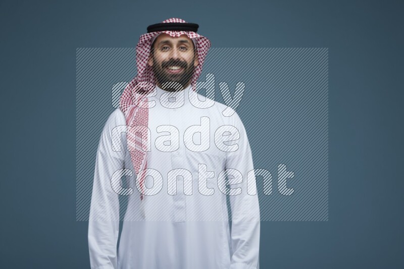 A man posing in a blue background wearing Saudi Thob and Shomag