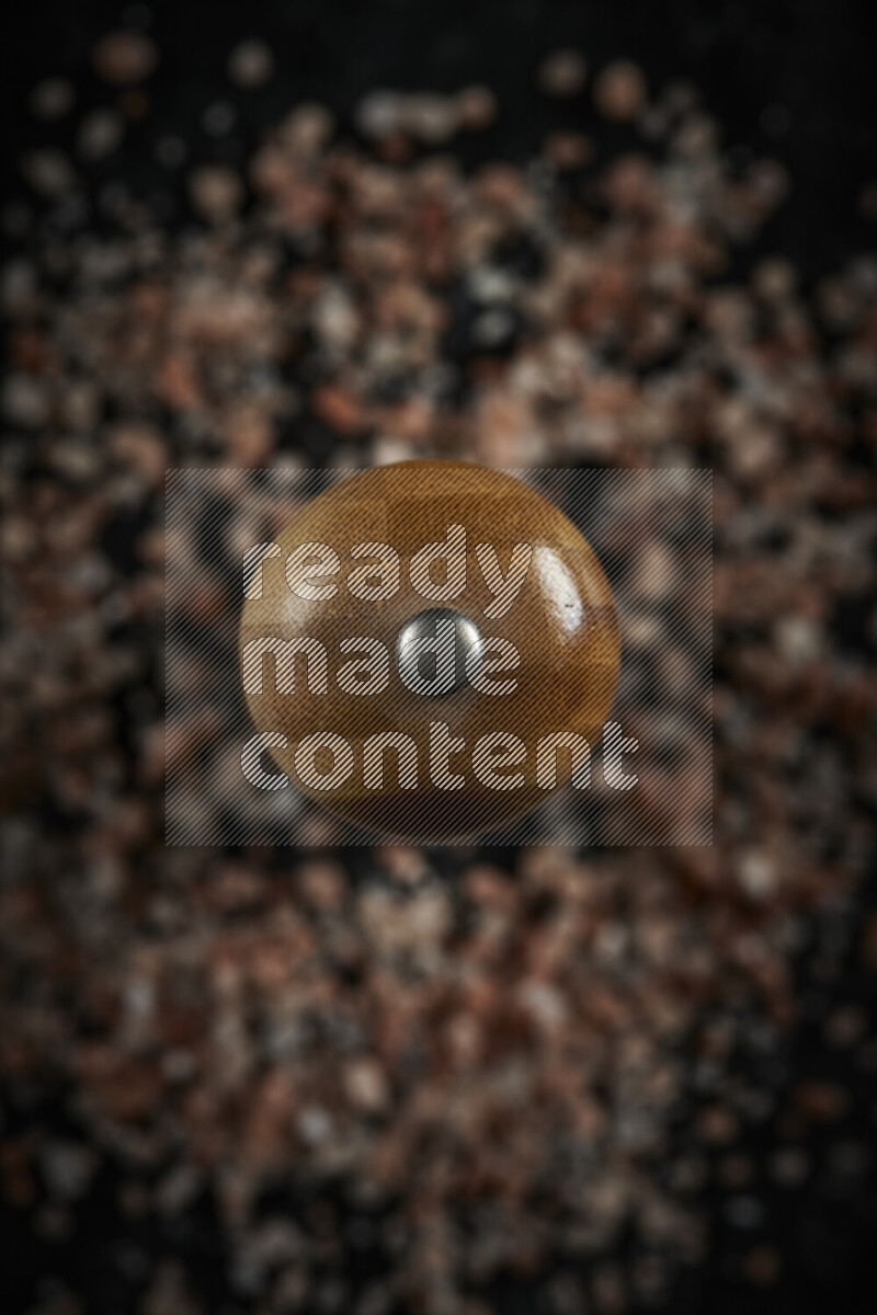 A wooden grinder standing upright and surrounded by coarse pink himalayan salt on black background