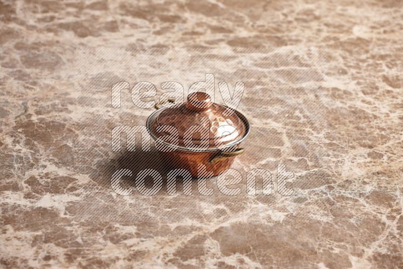 A small copper pot on beige marble background