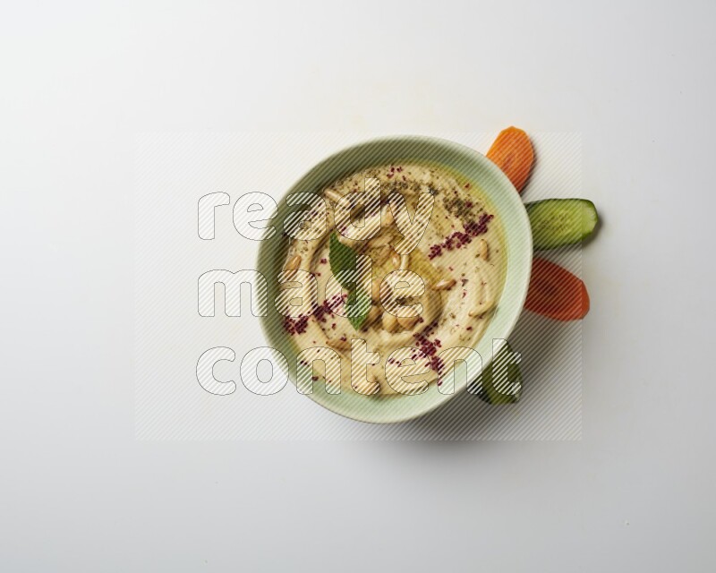 Hummus in a green plate garnished with zattar & sumak on a white background